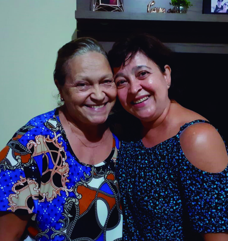Prela. Miriam e mae Reconciliar-se com os pais é a fonte da felicidade Olá! Meu nome é Mirian Regina Silva Fontes; conheci a Seicho-No-Ie em 1988, na cidade de Mogi-Guaçu, minha cidade natal, localizada no interior do estado de São Paulo. Sou Preletora da Seicho-No-Ie há 25 anos, e atualmente trabalho na Superintendência da Associação Pomba Branca da SEICHO-NO-IE DO BRASIL, como Coordenadora da Equipe Centro-Oeste e do Departamento Infantil e Kodomokai da SEICHO-NO-IE DO BRASIL. Venho compartilhar minha história de felicidade, conquistada graças às práticas do Ensinamento da Seicho-No-Ie em minha vida.
Sempre fui uma pessoa religiosa, sempre gostei de rezar. Porém, quando mais jovem, nutria um sentimento de revolta contra Deus. Isso porque, quando estava com 7 anos de idade, minha mãe resolveu sair de casa para viver com outra pessoa, deixando a mim, meu pai e meus dois irmãos. Para ajudar na criação dos filhos, meu pai optou por morarmos com meu avô paterno, que era um homem muito bravo, muito rígido. Nós três, como todas as crianças, corríamos durante as brincadeiras em casa e fazíamos os barulhos naturais da vida na infância, mas esse meu avô não tinha paciência e acabávamos apanhando sempre. Apanhamos muito. Cresci profundamente triste, porque quando apanhávamos eu pensava que, se minha mãe não tivesse ido embora, nós não estaríamos passando por aquilo. Eu queria ter aquela mãe amorosa que eu ouvia minhas amigas comentando, mas a minha não estava ali. Fui nutrindo sentimento de ódio pela minha mãe, pois me sentia lesada pela conduta dela.
A vida foi passando, e eu cresci com esses sentimentos de tristeza e revolta. Pensava que tinha nascido para ser infeliz e que assim seria até o fim. Quando estava com 20 anos, comecei a trabalhar num banco e uma querida amiga do trabalho me deu uma revista da Seicho-No-Ie. Lá estava escrito que podemos ser felizes, mediante nossa transformação. Identifiquei-me prontamente com o Ensinamento, me apaixonei por ele, e passei a frequentar as reuniões da Seicho-No-Ie na Associação Local da minha cidade. Aprendi diversas coisas maravilhosas nessas reuniões, entre elas o Ensinamento que consta na Revelação Divina da Grande Harmonia, do livro Revelações Divinas (Masaharu Taniguchi, 1ª ed., 2012, p. 13). Essa Revelação orienta que devemos ser gratos aos pais, pois quem não é grato aos pais não está em conformidade com a vontade de Deus. Entendi que precisava resolver essa questão com a minha mãe.
Passei a fazer a Oração para Reconciliar, que consta no livreto “Shinsokan e outras orações- Meditação para Contemplar a Deus ”(Masaharu Taniguchi, 37ª impr., 2010, p. 34), mas mesmo assim não conseguia transformar o ódio em amor. Continuei frequentando as reuniões, e mesmo depois de alguns anos na Seicho-No-Ie continuava da mesma forma. Até que fui participar de um Seminário de Treinamento Espiritual na Academia Sul-Americana de Treinamento Espiritual da Seicho-No-Ie de Ibiúna – SP. Os seminários da Seicho-No-Ie nas academias oferecem vivências, palestras e práticas que nos auxiliam muito na transformação interior que buscamos. Neste seminário, durante uma palestra do Preletor Ênio Maçaki Hara, tomei a decisão de me reconciliar com a minha mãe. Essa questão em aberto estava atrapalhando várias coisas em minha vida. Os pais são como portas para a felicidade. Quando temos amor por eles, encontramos tudo que precisamos na vida. Porém, quando mantemos sentimentos desarmoniosos com relação a eles, ainda que tenhamos razão para isso, as “saídas” para a vida parecem estar fechadas.
Nessa época, estava morando com a minha mãe, exatamente para resolver todas essas questões.  Apesar de ter tomado a decisão de perdoar, ainda não conseguia sentir amor. Então, fui participar de outro seminário, o Seminário para Jovens Mulheres, realizado pela Associação dos Jovens da SEICHO-NO-IE DO BRASIL (AJSI/BR). Este seminário é tradicionalmente realizado durante o feriado de Páscoa. Dediquei todas as práticas daquele seminário para o objetivo de me reconciliar com a minha mãe. Quando retornei, tomei coragem, joguei a mala num canto e fui procurar minha mãe. Encontrei-a lavando louça, na pia da cozinha. Ajoelhei-me no chão, abracei os pés dela, e pedi perdão, do fundo do coração. Foi emocionante. Ficamos abraçadas ali, durante uns 10 minutos, e pela primeira vez conversamos sobre os motivos que a levaram a sair da nossa vida naquela época. Só então pude conhecer sua versão da história e entender os sentimentos dela. Justamente num Domingo de Páscoa, data que representa renascimento e libertação, realmente renasci. Daquele momento em diante, toda a minha vida mudou. Com a minha reconciliação, meus irmãos também se reconciliaram com ela; a prosperidade surgiu em nossa vida e logo depois conheci minha alma gêmea, com quem hoje tenho duas filhas maravilhosas e sou plenamente feliz.  Estamos casados há 24 anos.
Sou testemunha de que o amor tudo cura, tudo resolve. Não é fácil nos ajoelharmos diante de alguém que até então odiávamos, que nos causou algum sofrimento e que por isso nos julgamos na posição de quem tem razão. Porém, a vida não é tão simples, e como seres humanos todos nós erramos vez ou outra, de modo que precisamos aprender a nos perdoar e a perdoar as outras pessoas também. Precisamos tomar a iniciativa de compreender o outro, especialmente nossos pais, pois enquanto não nos reconciliamos e não curamos os sentimentos de raiva, de mágoa, ficamos amarrados na situação e não conseguimos evoluir em todos os sentidos. Isso é necessário mesmo que eles não estejam mais neste plano.
Para quem estiver passando por uma situação de desarmonia com os pais, aconselho a fazer uma reflexão e tomar a decisão de perdoar. Isso fará bem a você e toda a família. Mesmo que não sejam os pais biológicos, na Seicho-No-Ie aprendemos que os pais adotivos são nossos pais também, assim designados por Deus para cumprir essa missão conosco. Eles merecem nossa total gratidão. Os pais biológicos também merecem profunda gratidão porque nos trouxeram à vida. Quando conseguimos amar, principalmente os pais, tudo se transforma; nossa vida passa a ter um rumo positivo, conseguimos conquistar a felicidade e encontrar a paz, que é a conquista mais importante de todas. Muito obrigada! Reuniões da Seicho-No-Ie para crianças em idioma japonês