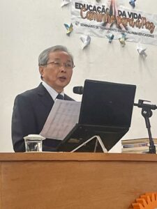 Professor Fumio Nishiyama, atrás do púlpito com o notebook e microfone proferindo uma palestra